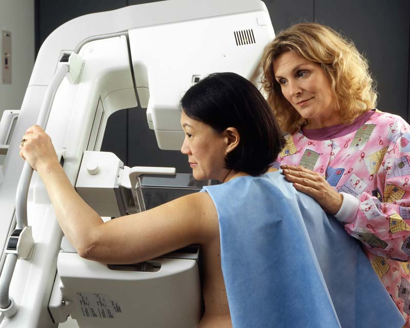 Woman holding on to mammography machine while nurse adjusts her